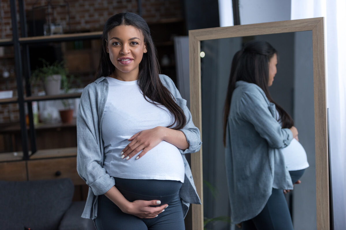 african american pregnant woman with big belly standing at mirror