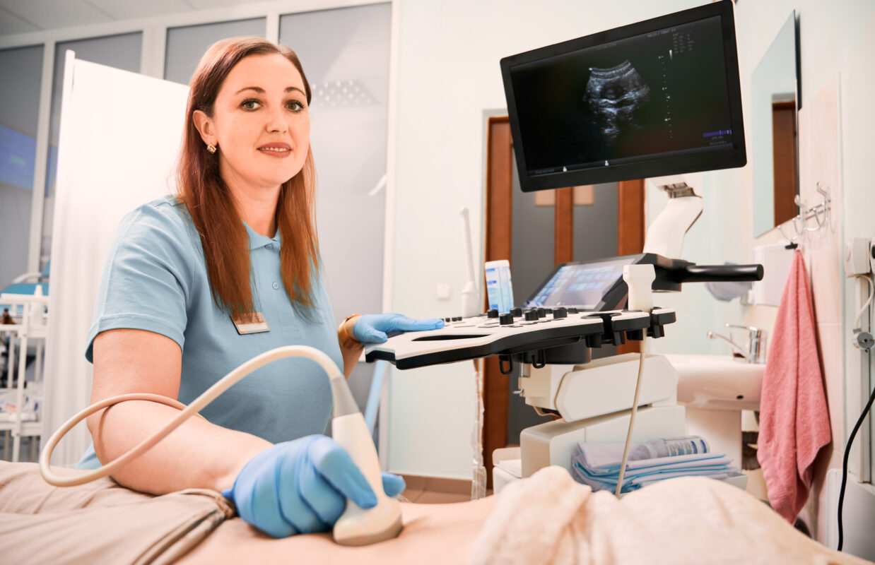 Woman sonographer in sterile gloves examining patient with ultrasound scanner. Portrait of female doctor doing ultrasound examination. Concept of healthcare, sonography and ultrasound diagnostics.